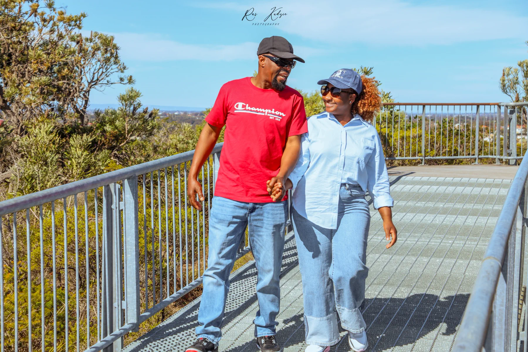 A couple walking hand in hand across a sunny lookout