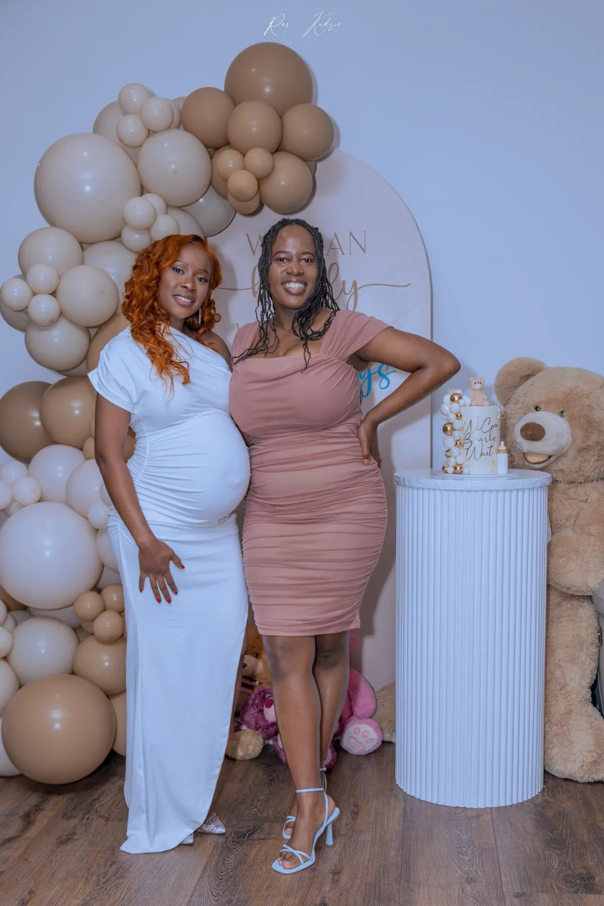 Expectant mother posing with a friend beside the balloon display