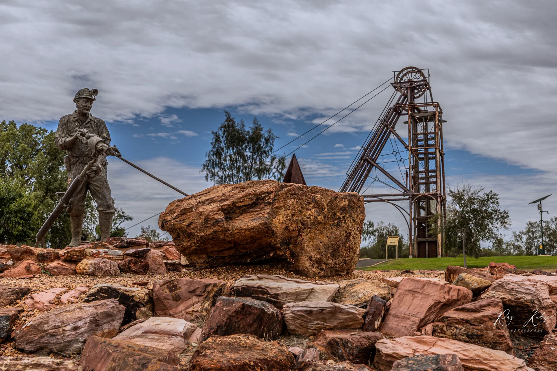 A miner statue and historic headframe framed by rust-coloured stone