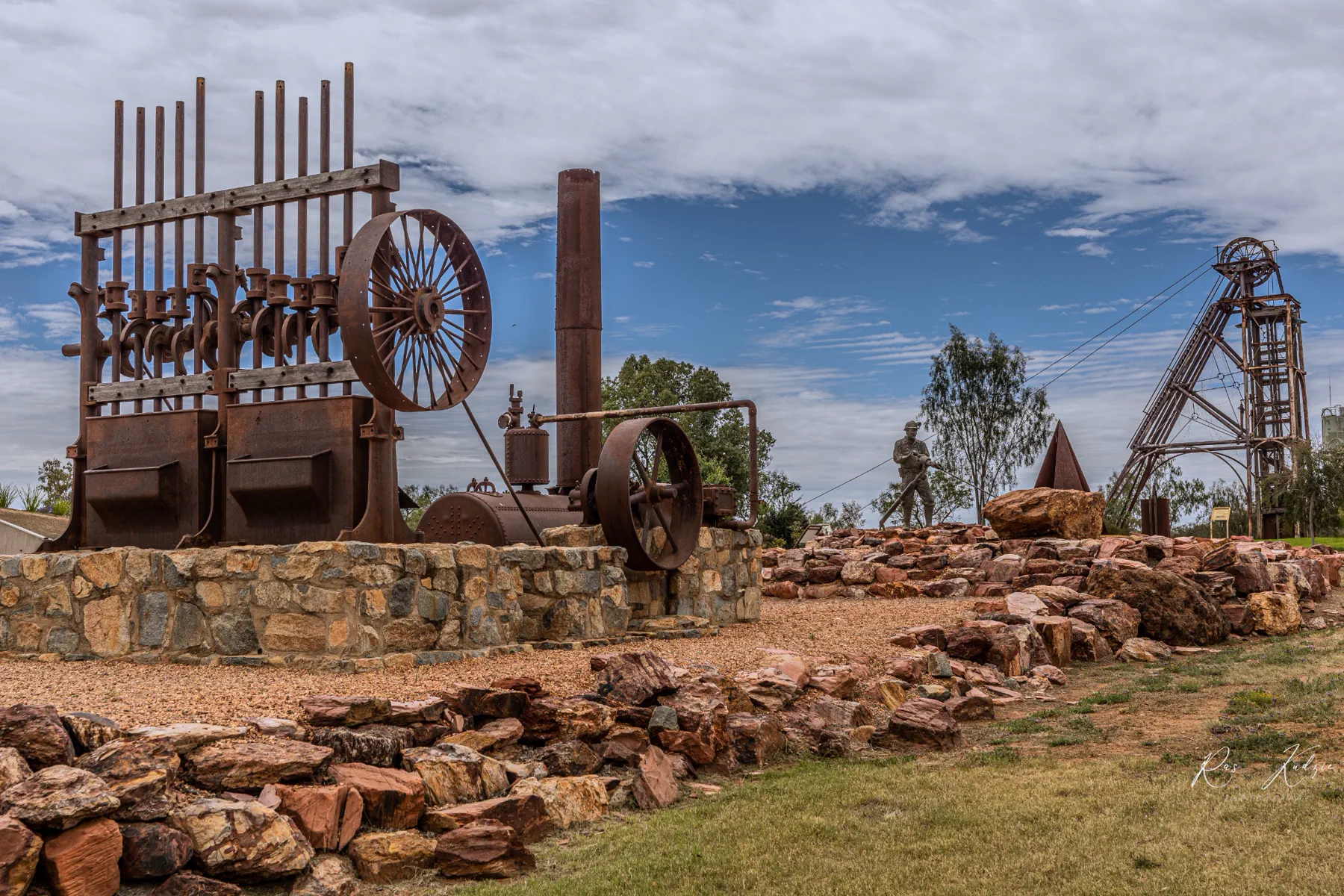 Historic mining machinery and headframe beneath broken cloud