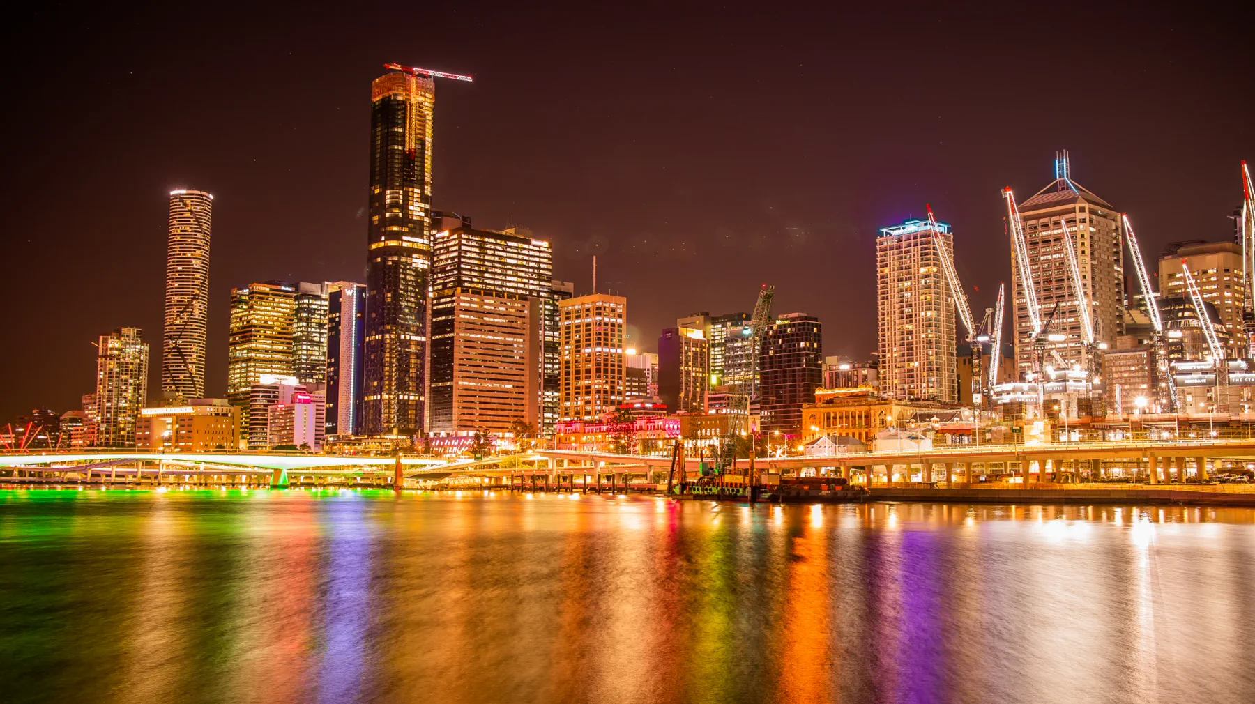 Brisbane city skyline glowing above colourful reflections on the river at night