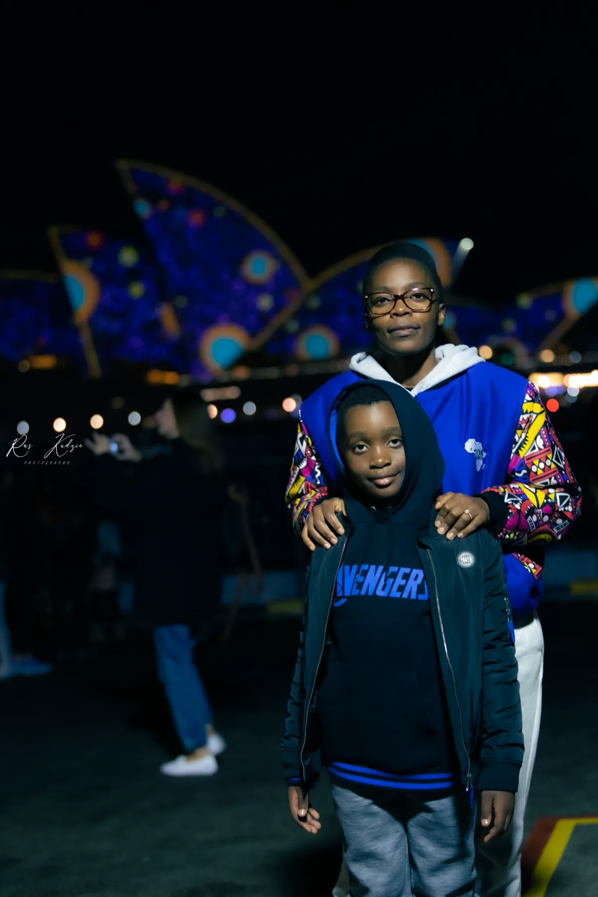 A mother and child photographed in front of the illuminated Sydney Opera House during Vivid Sydney