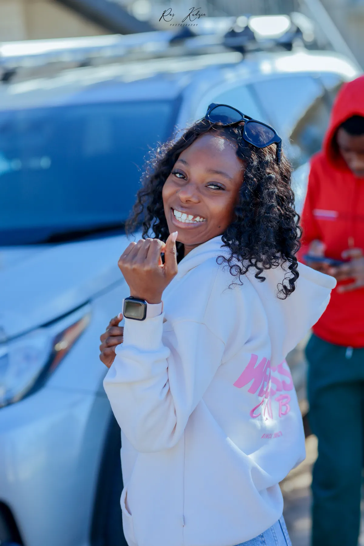 A smiling young woman turning toward the camera in a white hoodie